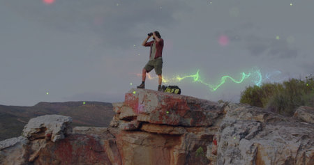 Scanning hiker wearing wide-brimmed hat on cliff with binoculars, backpack. Adventure, exploration,...