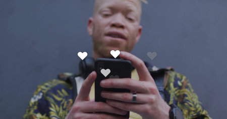 Man in floral jacket over ear headphones holding smartphone at gray wall, with floating heart icons....