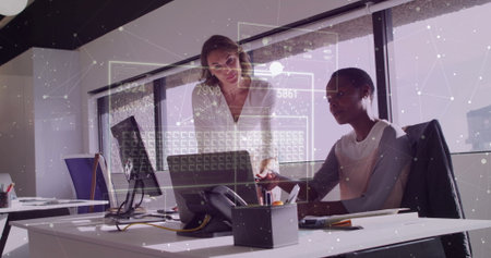 Leaning women wearing business attire pointing at laptop screen and typing in office with documents....
