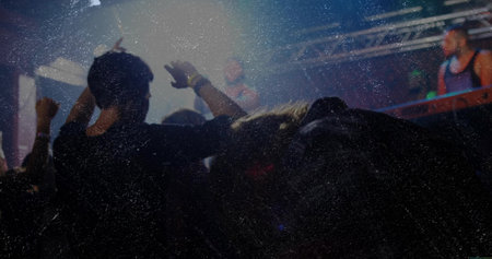 Raising arms concert crowd in dark T-shirts dancing at nightclub, with DJ console and stage lights. Stadium, festival, music, nightlife, entertainment, clubbing, vibrantの写真素材