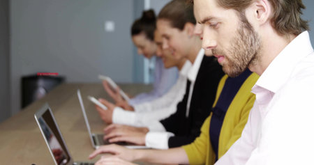 Typing man with beard wearing white shirt using laptop at modern conference room table, copy space. Collaboration, technology, workspace, innovation, professional, communication, minimalistの写真素材