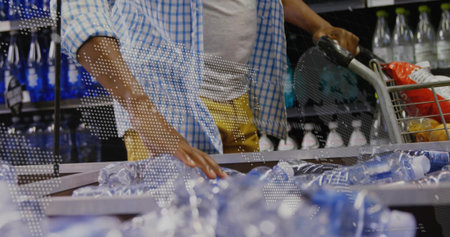Sorting male shopper selecting plastic water bottles in store aisle, with groceries in metal cart....