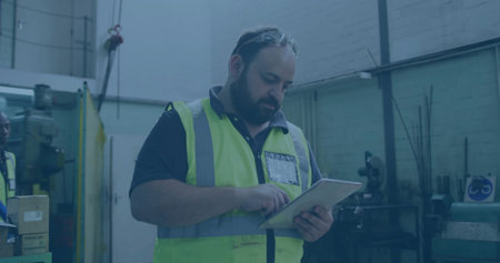 Technician wearing safety gear tapping tablet in workshop with drill press, storage boxes....