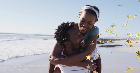Man carrying partner piggyback and strolling on beach by ocean waves, with golden star graphics....