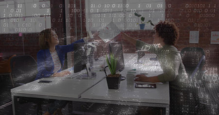 Fist bumping woman and man celebrating work in open-plan office, with dual monitors and succulent. Collaboration, teamwork, professional, modern, workspace, productivity, communicationの写真素材