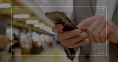 Holding smartphone man in suit jacket scrolling through device in public terminal, overhead lights....