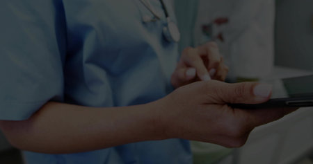 Using stylus clinician wearing blue scrubs interacting with tablet in clinic room, with stethoscope. Medical, clinical, technology, diagnostics, professionalism, healthcare, modernの写真素材