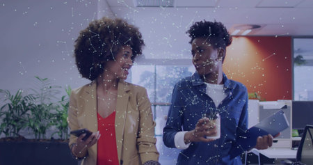 Walking women in blazers smiling holding smartphone and tablet in office hallway, network graphics. Collaboration, networking, innovation, modernity, communication, productivity, technologyの写真素材