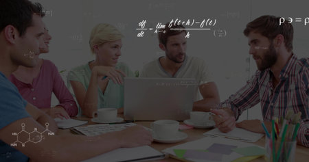 Leaning colleagues reviewing charts around wooden conference table in office, with silver laptop. Collaboration, teamwork, brainstorming, strategy, innovation, office, professionalの写真素材