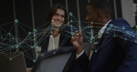 Discussing data Black man and white woman in suits at conference table with laptop, network overlay....