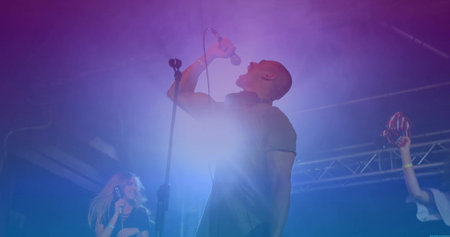 Gripping microphone singer belting out song on stage, with red maracas and colored LED lights. Performers, live music, concert atmosphere, stage lighting, musical collaboration, vibrant lightingの写真素材