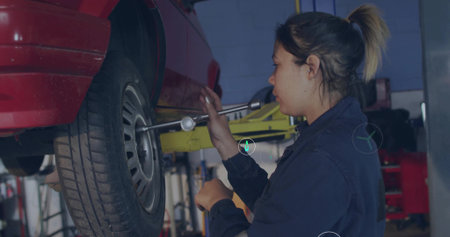 Using torque wrench, mechanic in coveralls tightening lugnut on car wheel in repair bay, copy space....