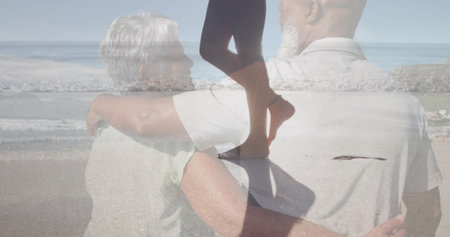 Embracing mature man and senior woman standing on sandy beach with walking silhouette in leggings. Romantic, serenity, vitality, silhouette, tranquility, connection, wellnessの写真素材