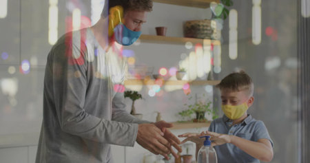 Guiding father and son wearing face masks practicing hand sanitizing on counter, with pump bottle. Family, hygiene, safety, warmth, education, environment, wellnessの写真素材