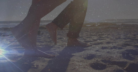 Stepping lower legs and feet across shoreline, with rolled-up pants, shoes, footprints, lens flare. Beach, romance, leisure, natural, relaxation, travel, lifestyleの写真素材