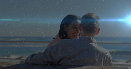 Leaning romantic couple hugging on wooden bench overlooking ocean horizon, with lens flare. Romance, connection, leisure, warmth, serenity, landscape, lifestyleの写真素材