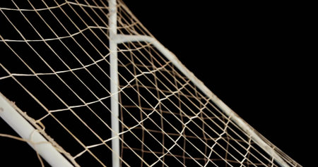 Displaying soccer goal corner with metal posts supporting diamond netting against black background....