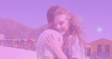 Hugging red-haired woman and striped tshirt man exchanging hug on sandy beach, with beach huts....
