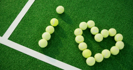 Displaying yellow tennis balls forming I heart shape on tennis court corner, with white court lines....