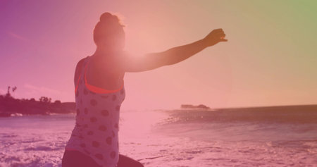 Balancing adult woman stretching on sandy shoreline, with gentle waves and sunlit horizon glow. Fitness, wellness, outdoor, serenity, mindfulness, silhouette, naturalの写真素材
