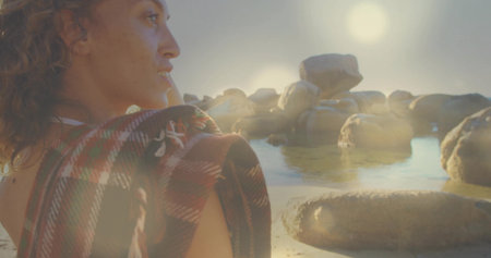 Standing female draping plaid blanket at rocky shoreline, with boulders and water, copy space. Seascape, leisure, tranquility, rustic, outdoor, reflection, naturalの写真素材