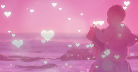 Standing mother and baby boy gazing at shoreline, with red bucket and heart overlays, copy space. Parenthood, bonding, seaside, sunset, tranquility, tenderness, childhoodの写真素材