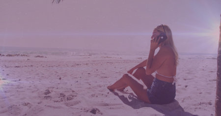 Talking woman using smartphone on beach in bikini top, denim shorts, palm tree trunk, copy space. Coastline, leisure, relaxation, outdoor, fashion, tropical, scenicの写真素材