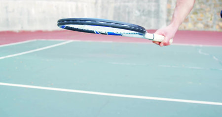Player's forearm gripping tennis racket on court with white lines, red perimeter, stone wall fence....