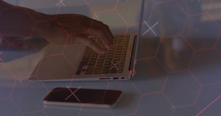 Hand wearing shirt typing on home desk with silver laptop smartphone and red hexagonal grid overlay. Technology, cybersecurity, digital, innovation, workspace, modern, connectivityの写真素材