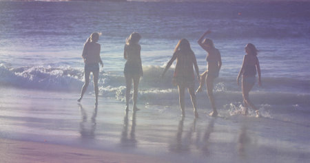 Standing five friends in summer clothes experiencing surf at beach, with ocean waves and wet sand. Seascape, companionship, leisure, serenity, silhouette, natural light, outdoorの写真素材
