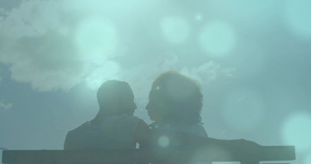 Leaning couple sharing moment on overlook wooden bench showing backlit silhouettes and lens flares. Romance, serenity, silhouette, appreciation, companionship, nature, tranquilityの写真素材