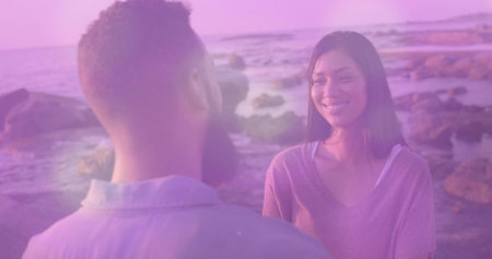 Smiling woman wearing sweater facing man on rocky beach with boulders, shallow water, copy space....
