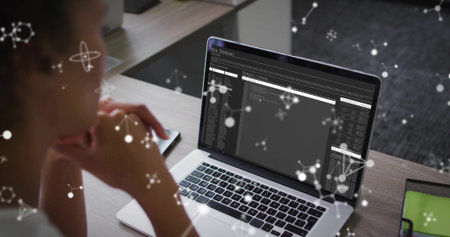 Reviewing mid adult woman examining terminal windows on laptop at workspace, with network overlays....