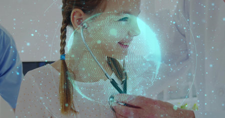 Lab coat doctor placing stethoscope on girl in clinic, with blue scrubs staff and hologram globe. Healthcare, pediatrics, innovation, technology, diagnostics, medicine, professionalismの写真素材