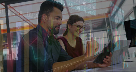 Reviewing professionals in business attire in open-plan office, overlaying digital graphs on tablet....