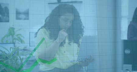 Analyzing seated woman wearing yellow blouse using tablet in open plan office, showing rising graph....