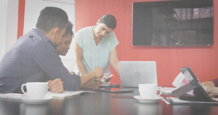 Collaborating professionals leaning over documents and devices at conference table, with coffee. Corporate, teamwork, modern, technology, discussion, brainstorming, productivityの写真素材