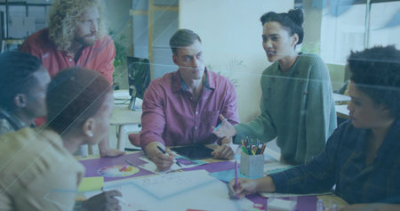 Discussing six colleagues reviewing sketches around table in workspace, with tablet and pencils. Collaboration, teamwork, brainstorming, innovation, contemporary, graphic design, productivityの写真素材