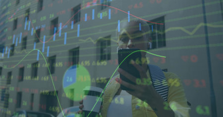 Checking smartphone while holding cup woman wearing jacket on city sidewalk, with stock charts....