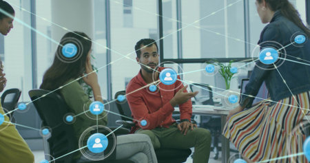 Gesturing diverse colleague wearing red shirt at office desk with monitors and network icons....