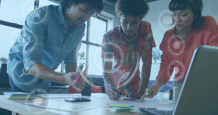 Collaborating three colleagues leaning over papers on table in office, with markers and overlay. Teamwork, innovation, brainstorming, communication, modernity, productivity, digitalの写真素材