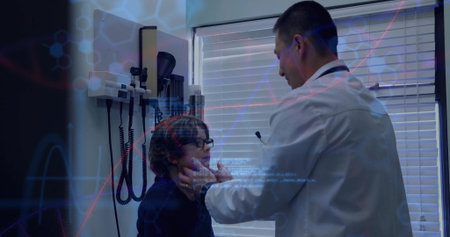 Asian doctor in white coat holding child's jaw and checking throat in exam room with stethoscope....