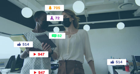 Colleagues wearing face masks standing in office, with tablet folder and social media icons. Collaboration, teamwork, digital, innovation, modernity, communication, productivityの写真素材