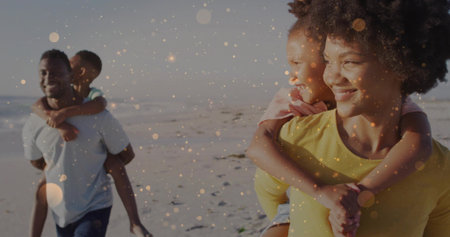 Walking family of four carrying children on backs along sandy beach at sunset, golden bokeh....
