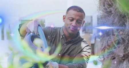Watering mid adult man nurturing leafy plants in greenhouse holding watering can and wearing gloves. Botanical, horticulture, verdant, wellness, natural, organic, nurturingの写真素材