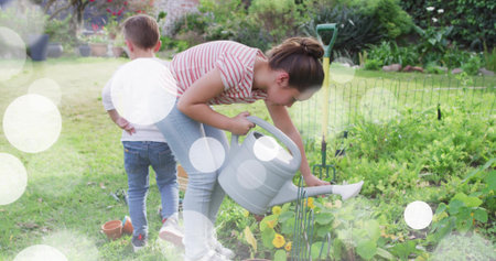 Girl pouring water while boy watching in backyard garden, with grey watering can. Gardening, family,...