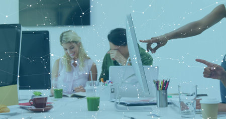 Collaborating colleagues reviewing documents around table in office with monitors and green juice. Teamwork, innovation, modern, digital, networking, productivity, creativeの写真素材