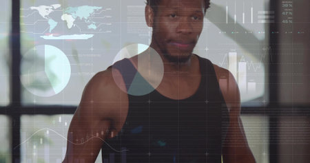 Standing male wearing black sleeveless shirt in gym, with world map, chart overlays on grid windows. Fitness, data visualization, modern infrastructure, technology, productivity, innovation, healthの写真素材