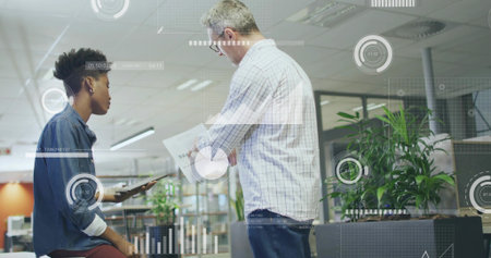 Reviewing tablet and papers, two colleagues meeting in open-plan office, with data overlays. Collaboration, teamwork, dataanalysis, productivity, modernoffice, professional, digitaltechnologyの写真素材