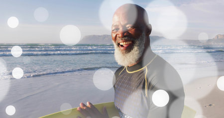 Grinning senior surfer wearing wetsuit and holding yellow surfboard on beach, copy space. Adventure,...
